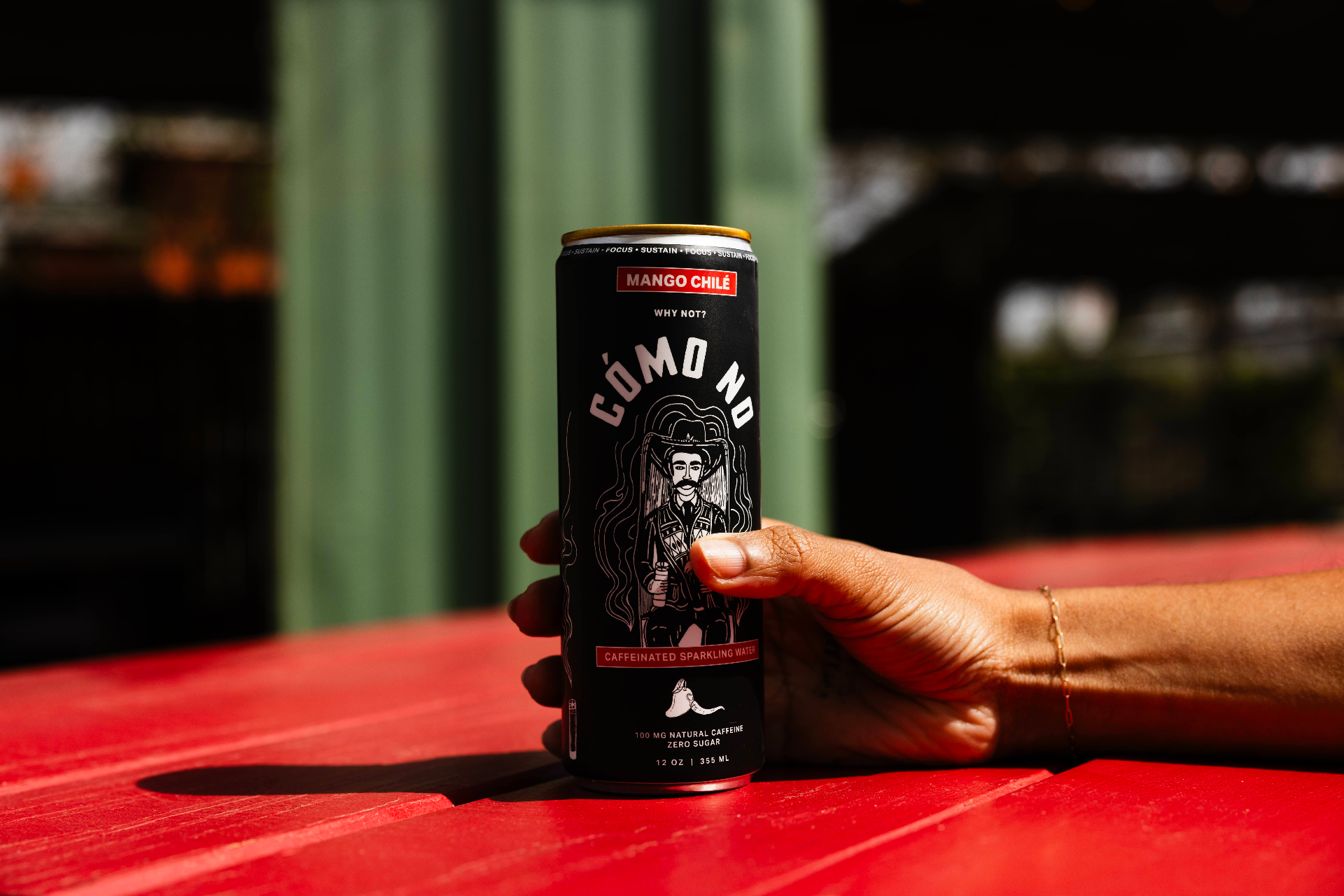 Cómo No Mango Chilé caffeinated sparkling water held above a red picnic table